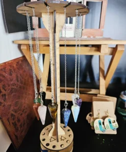 Wooden pendulum display stand with engraved sacred geometry and gemstone pendulums hanging from each slot.