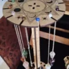 Wooden pendulum holder with multiple crystal pendulums hanging on silver chains, shown on green glitter surface.