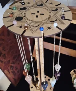 Wooden pendulum holder with multiple crystal pendulums hanging on silver chains, shown on green glitter surface.