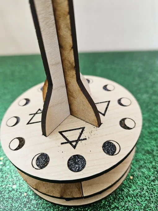 Close-up of wooden pendulum stand base engraved with moon phases and elemental symbols.