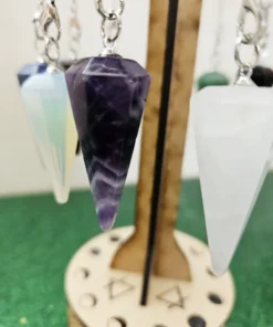 Close-up of amethyst pendulum hanging on metaphysical wooden stand with moon phase engraving.