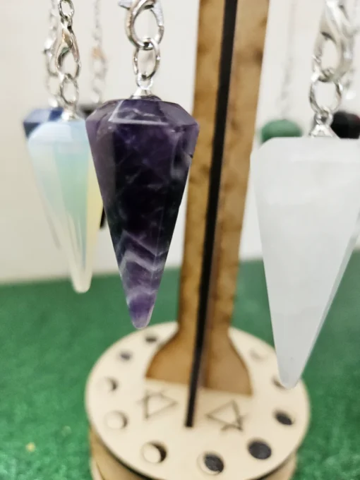 Close-up of amethyst pendulum hanging on metaphysical wooden stand with moon phase engraving.