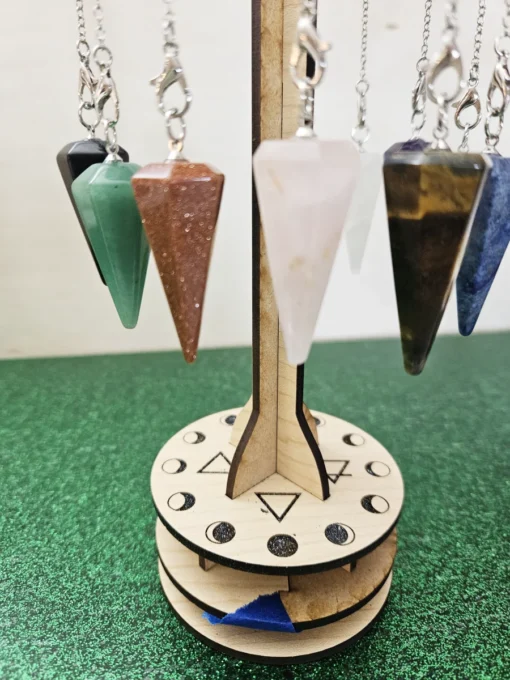 Assorted gemstone pendulums hanging on a wooden sacred geometry display stand.