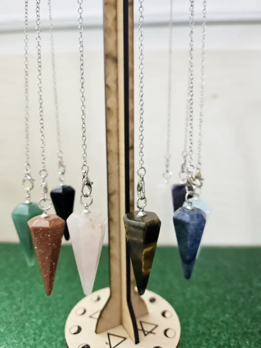 Various chakra crystal pendulums shown hanging evenly on custom engraved wood stand.