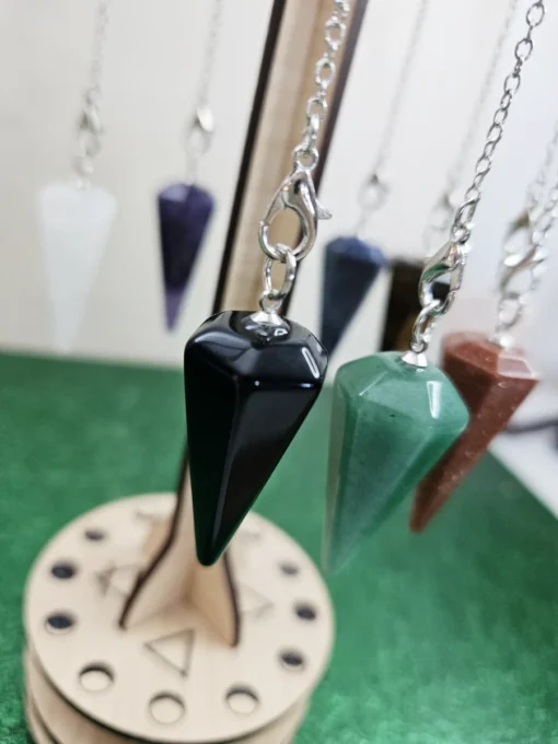 Close-up of natural gemstone pendulums, including rose quartz and tiger’s eye, on a moon phase engraved stand.