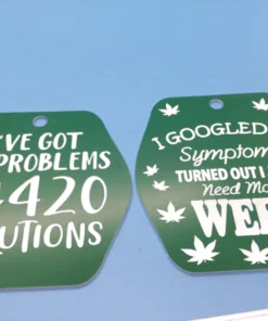 A set of green and white plastic keychains with laser-etched weed quotes, including “99 Problems & 420 Solutions” and “I Just Need More Weed.” These can also be used as magnets.