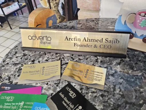 Custom gold metallic desk name plate with CEO title and business logo, displayed with matching business cards.