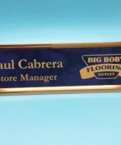 Custom blue and gold engraved name plate with store manager title and business logo, displayed on a bright blue background.