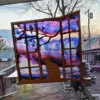 Stained-glass style suncatcher with a silhouette of a cat sitting at a window, gazing at a purple and pink sunset sky with tree branches in the foreground.
