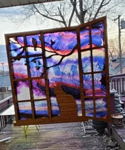 Stained-glass style suncatcher with a silhouette of a cat sitting at a window, gazing at a purple and pink sunset sky with tree branches in the foreground.